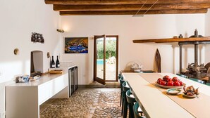 A dining area with a stone-tiled floor, a long table, and a view of the outdoors through a glass door. - Gia Costa - Eight Bedroom Villa, Sleeps 16 (Buseto Palizzolo)