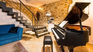 A living room with a grand piano, a blue sofa, a staircase with stone walls, and a small table. - Gia Costa - Eight Bedroom Villa, Sleeps 16 (Buseto Palizzolo)