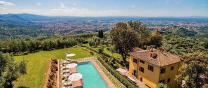 A villa with a swimming pool, surrounded by a well-maintained garden and overlooking a valley.