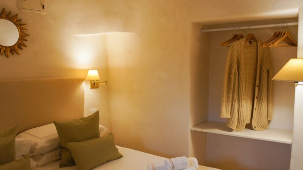 Een hotelkamer met een bed, kussens, een bedlamp, een kledingkast met hangers en een plank met handdoeken.