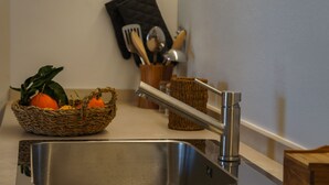 Een keukenkraan van roestvrij staal, een rieten mand met fruit, en een keukengerei houder op het aanrecht.