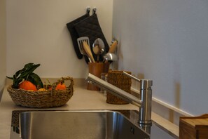 A kitchen sink with a stainless steel faucet, a woven basket with fruits, and a utensil holder on the countertop. - La Piccola Pietrina - One Bedroom Villa, Sleeps 2 (Ostuni)