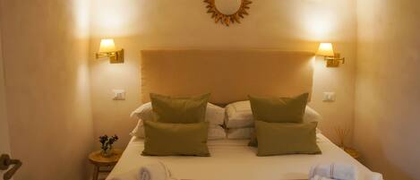 Habitación de hotel con una cama, dos lámparas de pared, un reloj de pared y una mesita con un florero y toallas.