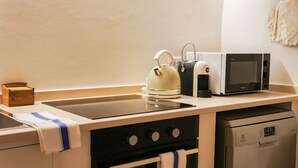 Een kleine keuken met een kookplaat, oven, magnetron en waterkoker.