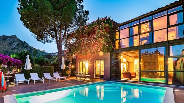 Ein modernes Haus mit Swimmingpool, einer Terrasse mit Liegestühlen und einem großen Baum.