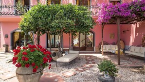 Ein pinkfarbenes Gebäude mit einer überdachten Terrasse, einem großen Pflanzgefäß mit roten Blumen und einem kleinen Baum.