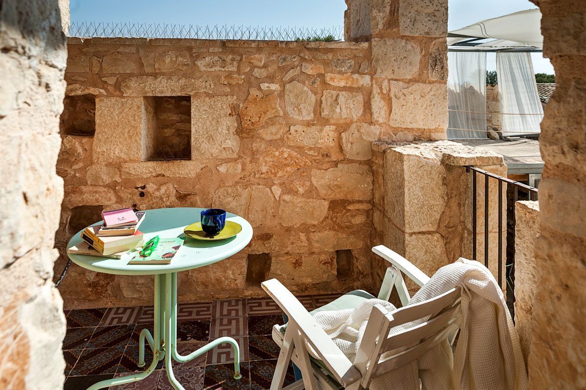Un espace extérieur aménagé avec des murs en pierre, comprenant une table et des chaises, une petite fenêtre et une vue sur une tente blanche en toile de fond.