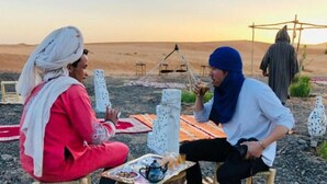 Two people sitting on a carpeted area outdoors with a table in front of them. - Fabulous Desert Camp (Merzouga)