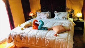 A hotel room with a large bed, floral-patterned pillows, and a decorative swan-shaped pillow. - Fabulous Desert Camp (Merzouga)