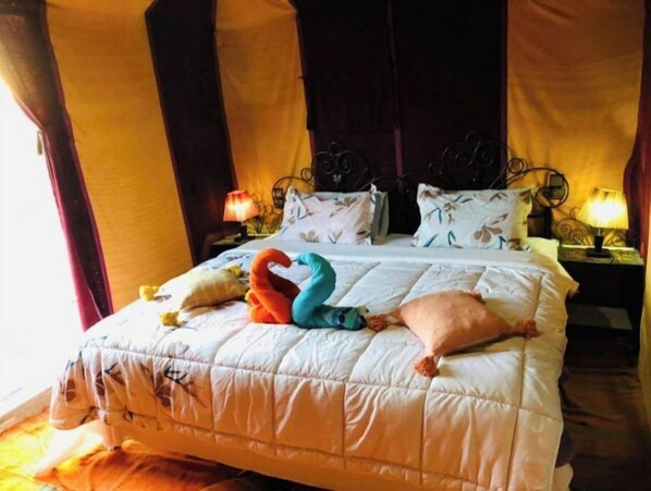 A hotel room with a large bed, floral-patterned pillows, and a decorative swan-shaped pillow. - Fabulous Desert Camp (Merzouga)