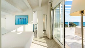 Een slaapkamer met een groot bed, een schilderij en uitzicht op zee vanaf een balkon.