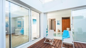 Een modern binnenzwembad met glazen wanden, houten terras en twee ligstoelen.