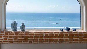 Een uitzicht door een boogvenster op zee, met een bakstenen vensterbank en decoratieve objecten.