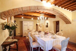 A dining room with a brick arch, white chairs, a table set for six, and a chandelier.