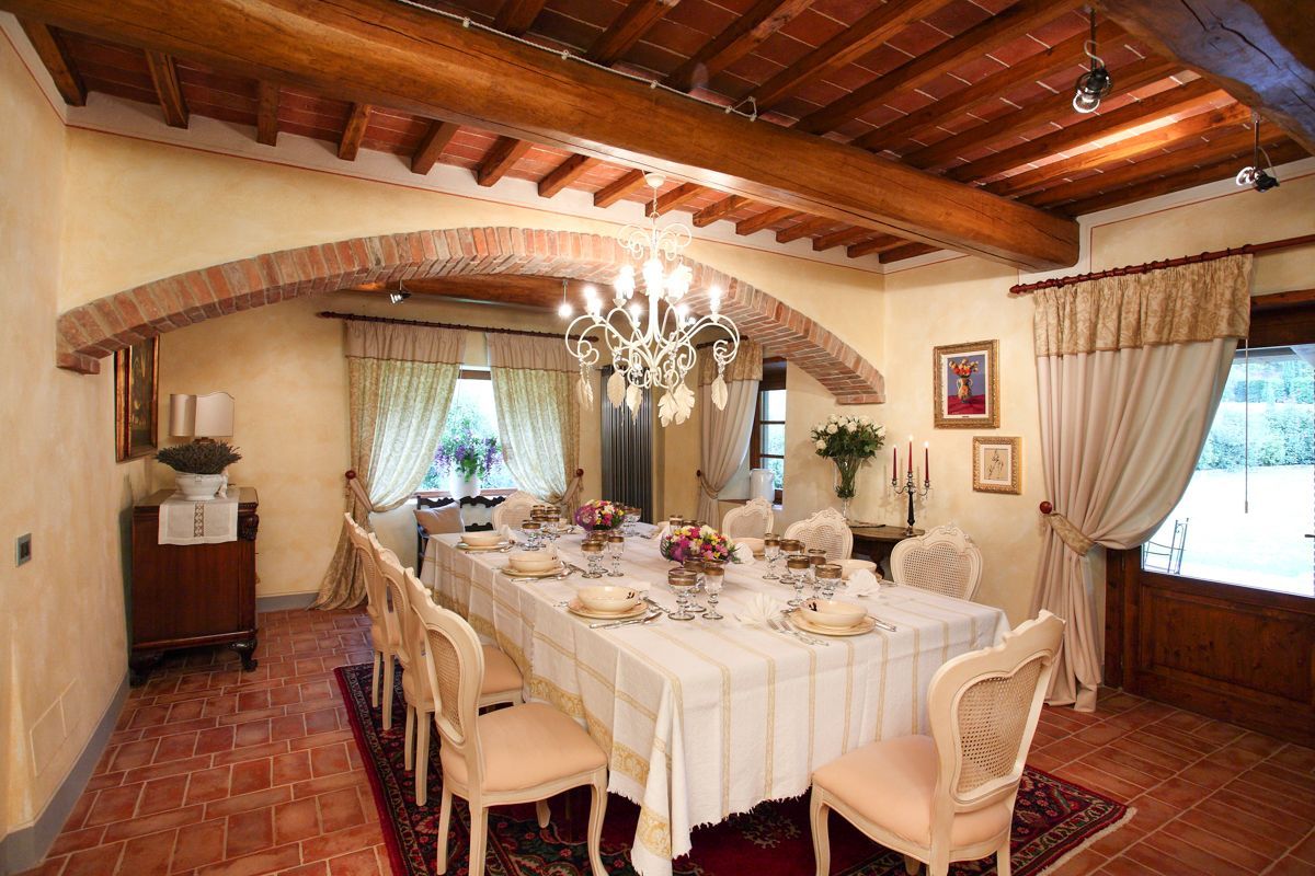 Une salle à manger avec une longue table dressée pour le repas, des poutres en bois au plafond et un lustre.