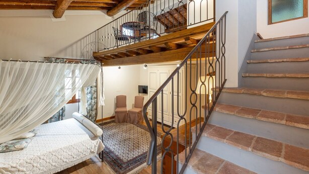 Ein Schlafzimmer mit Baldachinbett, einer Treppe mit schmiedeeisernem Geländer und Blick auf einen Balkon mit einem Stuhl.