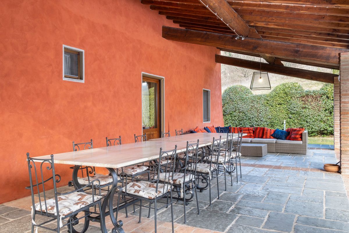 An outdoor dining area with a long table and chairs, a wooden ceiling, and a seating area with cushions.