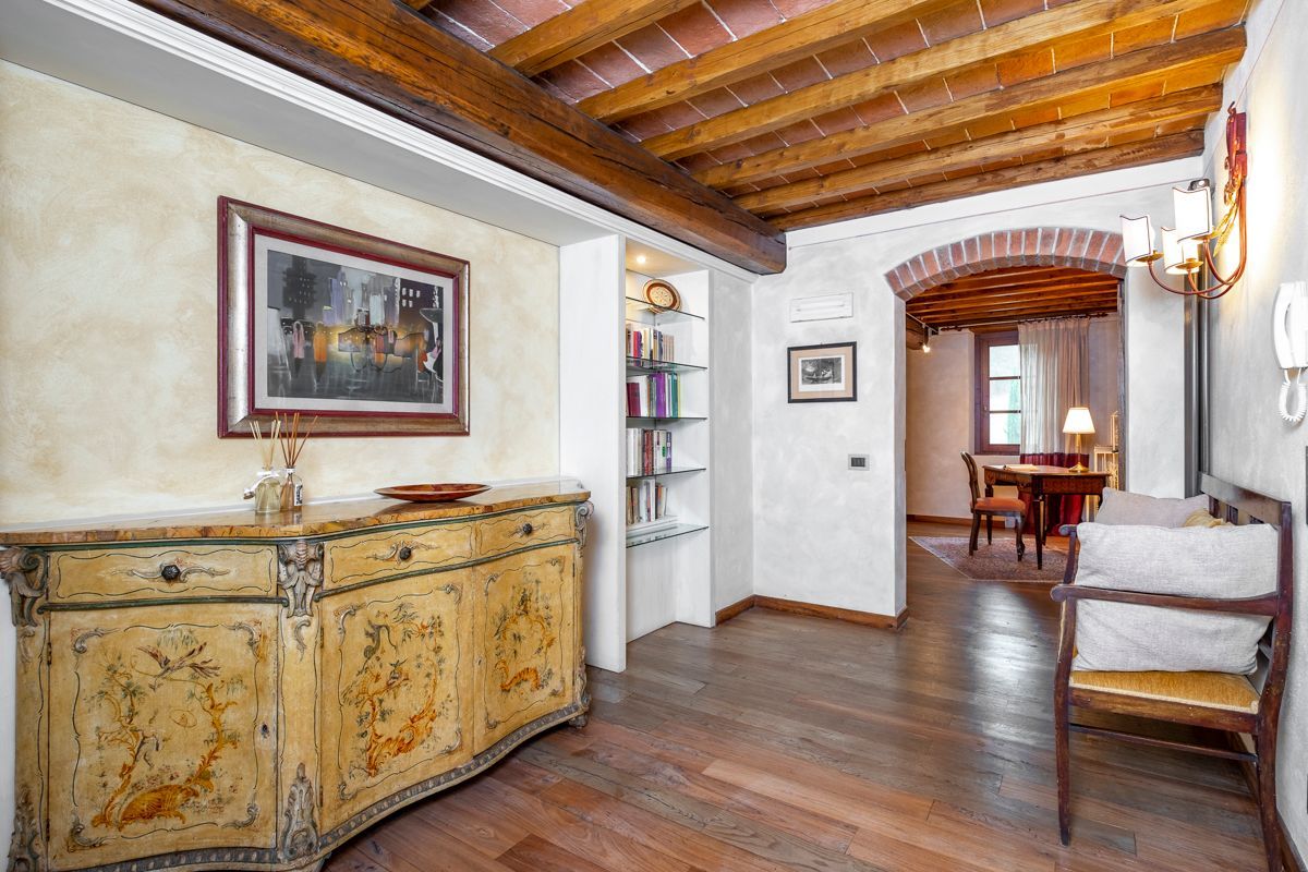 A room with a wooden ceiling, a vintage cabinet, a framed picture, a bookshelf, a dining area with a table and chairs, and a phone on the wall.