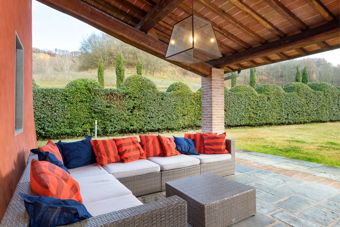 An outdoor seating area with a sofa and cushions, a table, and a pergola overhead.