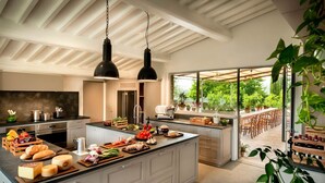 Une cuisine moderne dotée d’un grand îlot central, de luminaires suspendus et offrant une vue sur la terrasse extérieure.