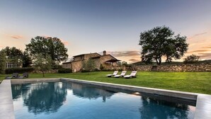 Une piscine avec des chaises longues, une maison en pierre et une pelouse verdoyante.