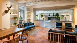Un vaste espace de vie comprenant un canapé bleu, une table à manger en bois et des chaises. Une tête de cerf est accrochée au mur. La cuisine est visible et est équipée d’appareils électroménagers modernes et agrémentée de plantes.