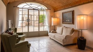 Une pièce chaleureuse avec une grande fenêtre en arc de cercle, un canapé, deux fauteuils, un tableau et deux lampadaires.