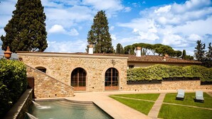 Un bâtiment en pierre doté d’une piscine, de fenêtres en arc de cercle et d’une pelouse bien entretenue.