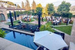 Evento al aire libre con escenario, asientos y piscina.