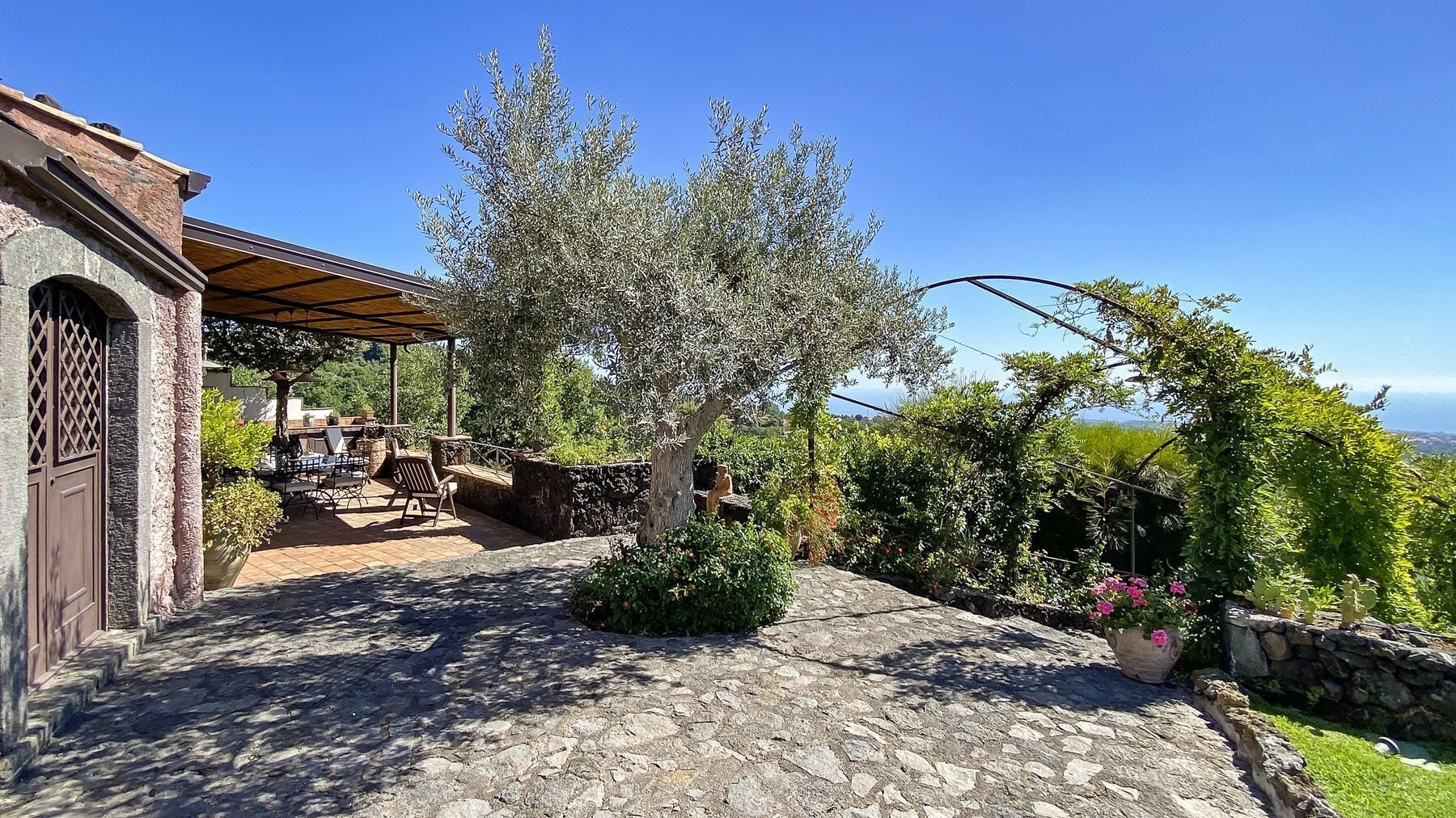 A stone-paved patio with outdoor furniture, a pergola, and a view of the countryside.
