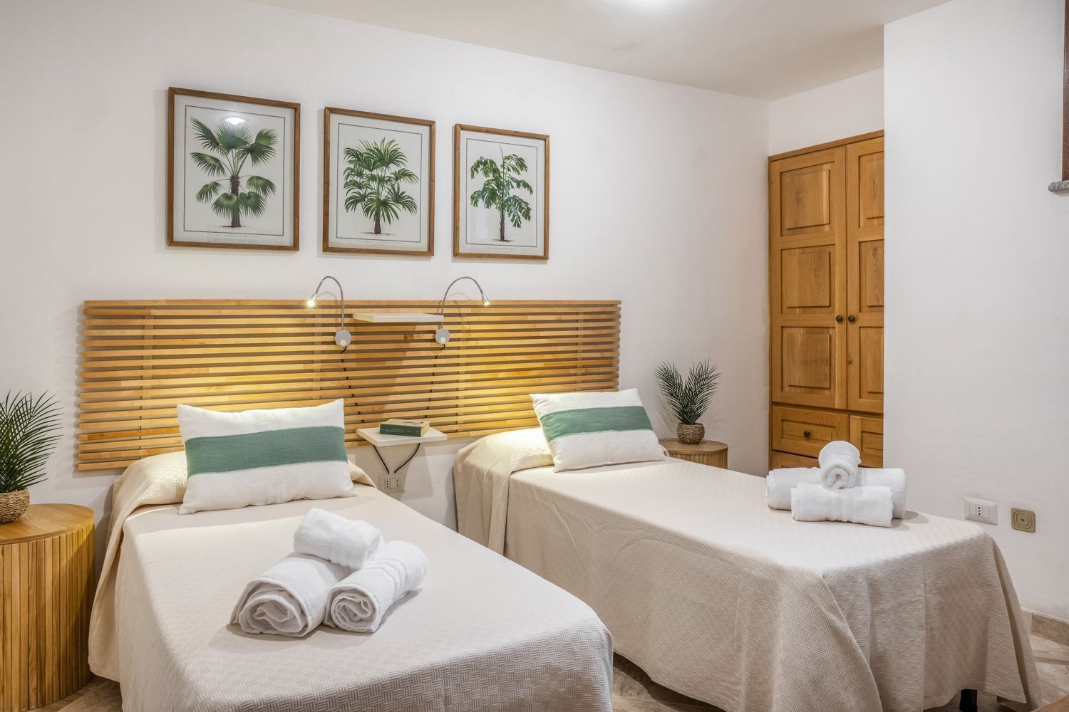 Quarto de hotel com duas camas, cabeceiras de madeira e quadro com tema de palmeiras na parede.