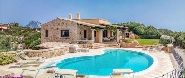 A stone house with a swimming pool, outdoor furniture, and a view of a mountain.