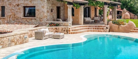 A stone building with a pool, outdoor seating, and a pergola.