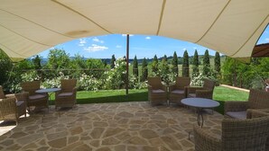 Eine Terrasse im Freien mit Korbmöbeln und Steinböden, umgeben von einem Garten mit verschiedenen Pflanzen und Bäumen.