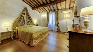Ein Hotelzimmer mit Bett, Holzboden, Decke mit freiliegenden Balken, Nachttisch mit Lampe und Kommode mit Lampe.