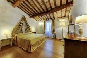 A hotel room with a bed, wooden flooring, a ceiling with exposed beams, a nightstand with a lamp, and a dresser with a lamp. - Villa Cecconi - Twelve Bedroom Villa, Sleeps 24 (Poggibonsi)