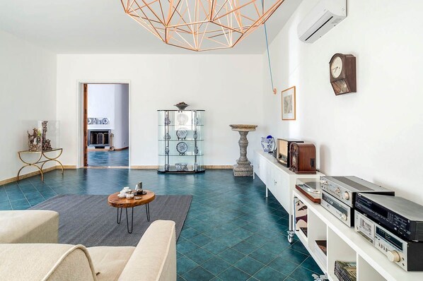 A modern living room with a geometric ceiling light, a glass display cabinet, and a vintage radio collection.