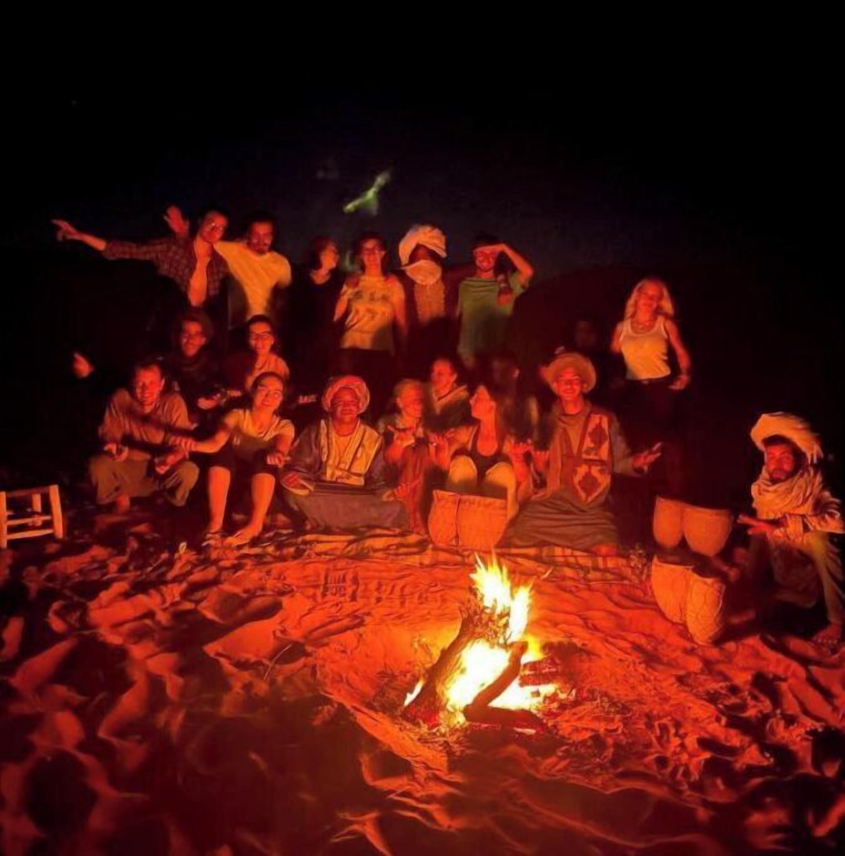 A group of people gathered around a campfire on a beach at night.