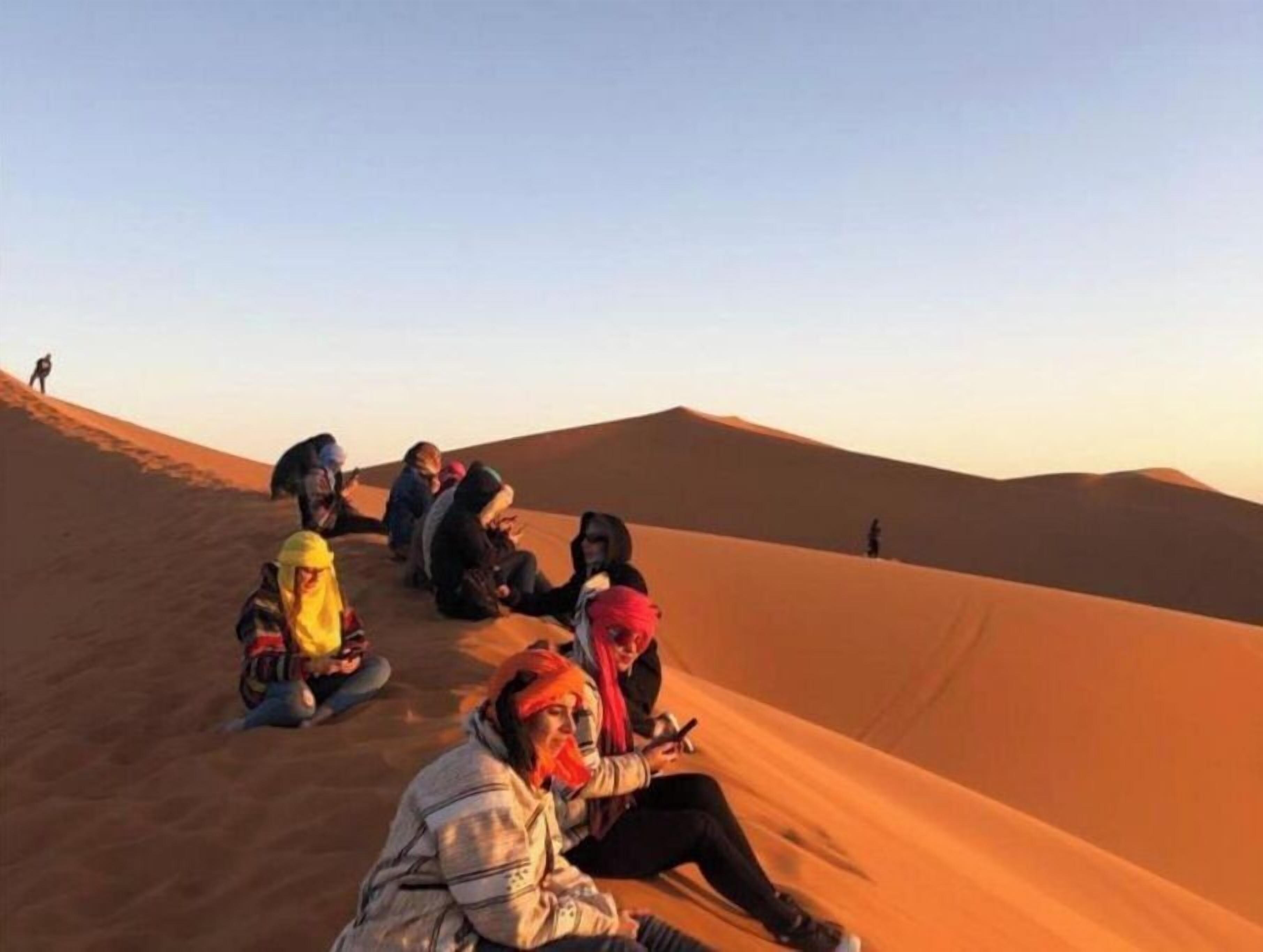 Un grupo de personas sentadas sobre una duna de arena en un paisaje desértico.