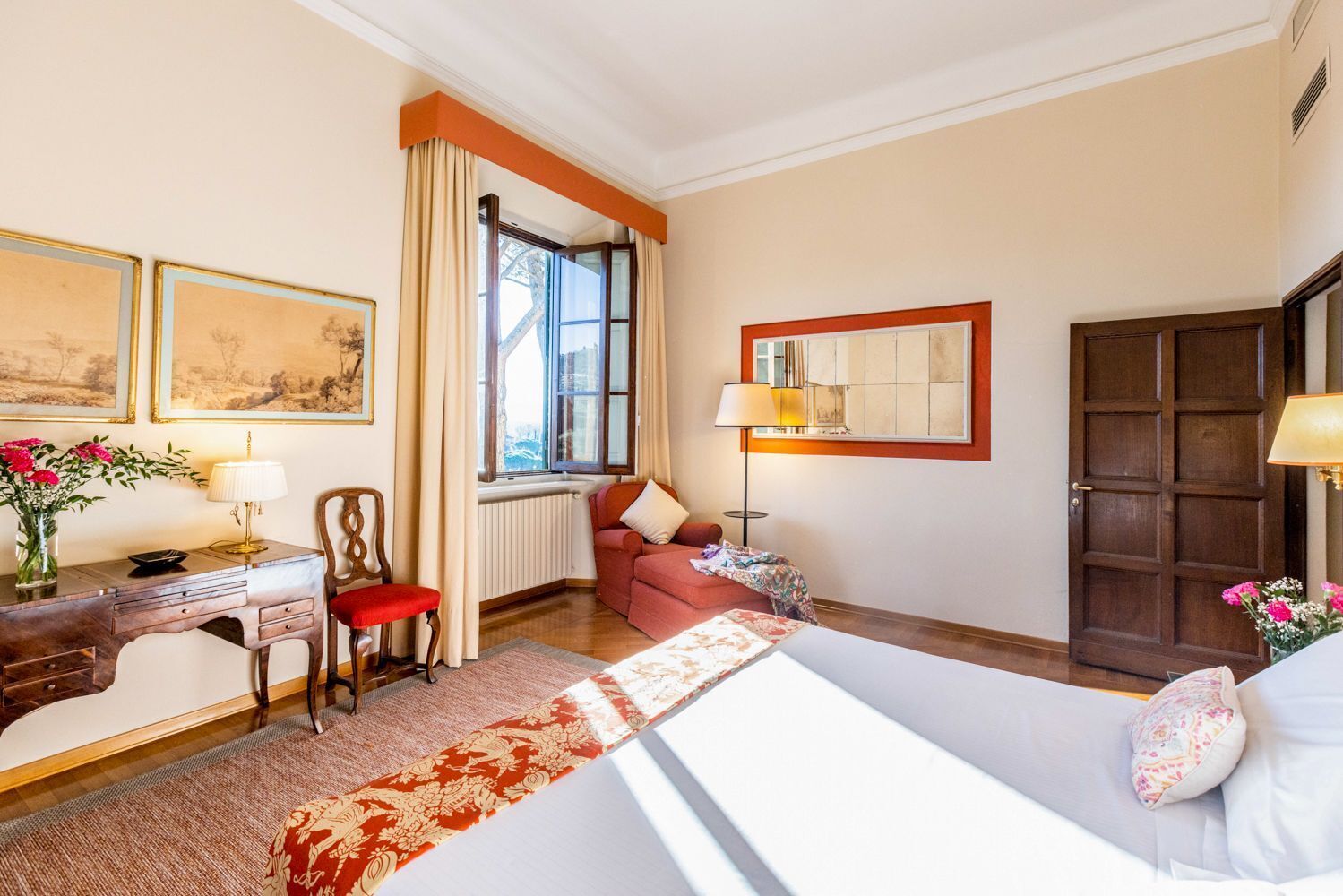 Une chambre d’hôtel comprenant un lit, un bureau avec une lampe, une chaise, un canapé, une fenêtre avec des rideaux et une porte.