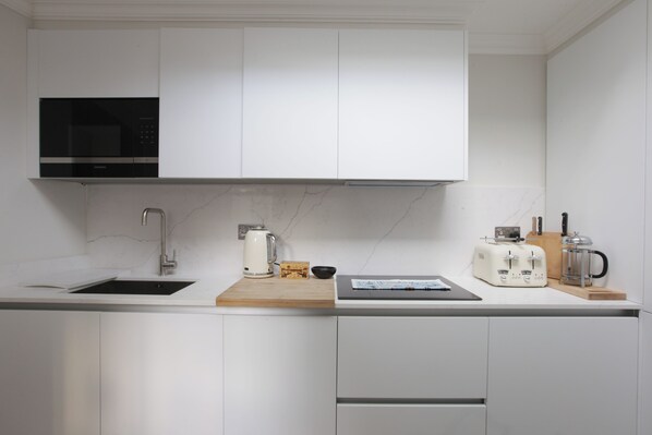 A modern kitchen with white cabinetry, a built-in microwave, a coffee maker, and a toaster.