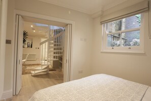A bedroom with a bed, a window with a view, a staircase, and a radiator. - Sleek 1BDR Retreat Near Portobello Road (London)