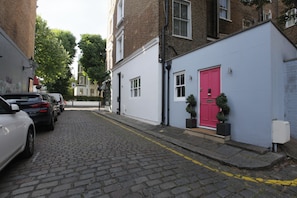 Une ruelle étroite pavée, avec des voitures garées d’un côté et une rangée de bâtiments dont la porte est peinte en rouge de l’autre côté.