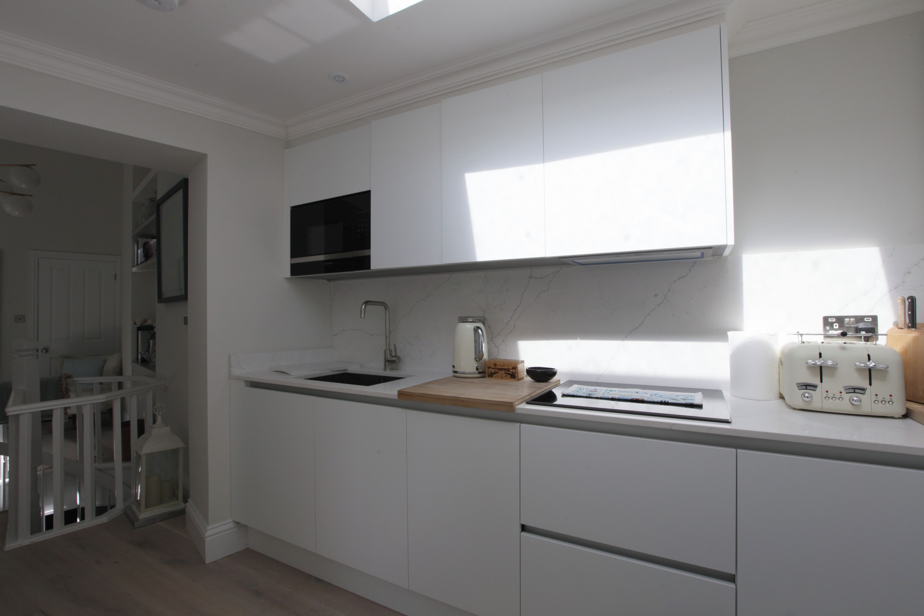 Una cocina moderna con armarios blancos, microondas integrado y encimera de madera.