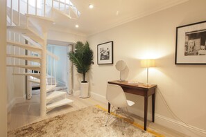 Un intérieur moderne avec un escalier, un bureau doté d’une lampe, une chaise et des tableaux encadrés accrochés au mur.