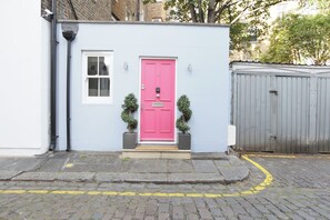 A building with a pink door, a small window, and two potted plants.