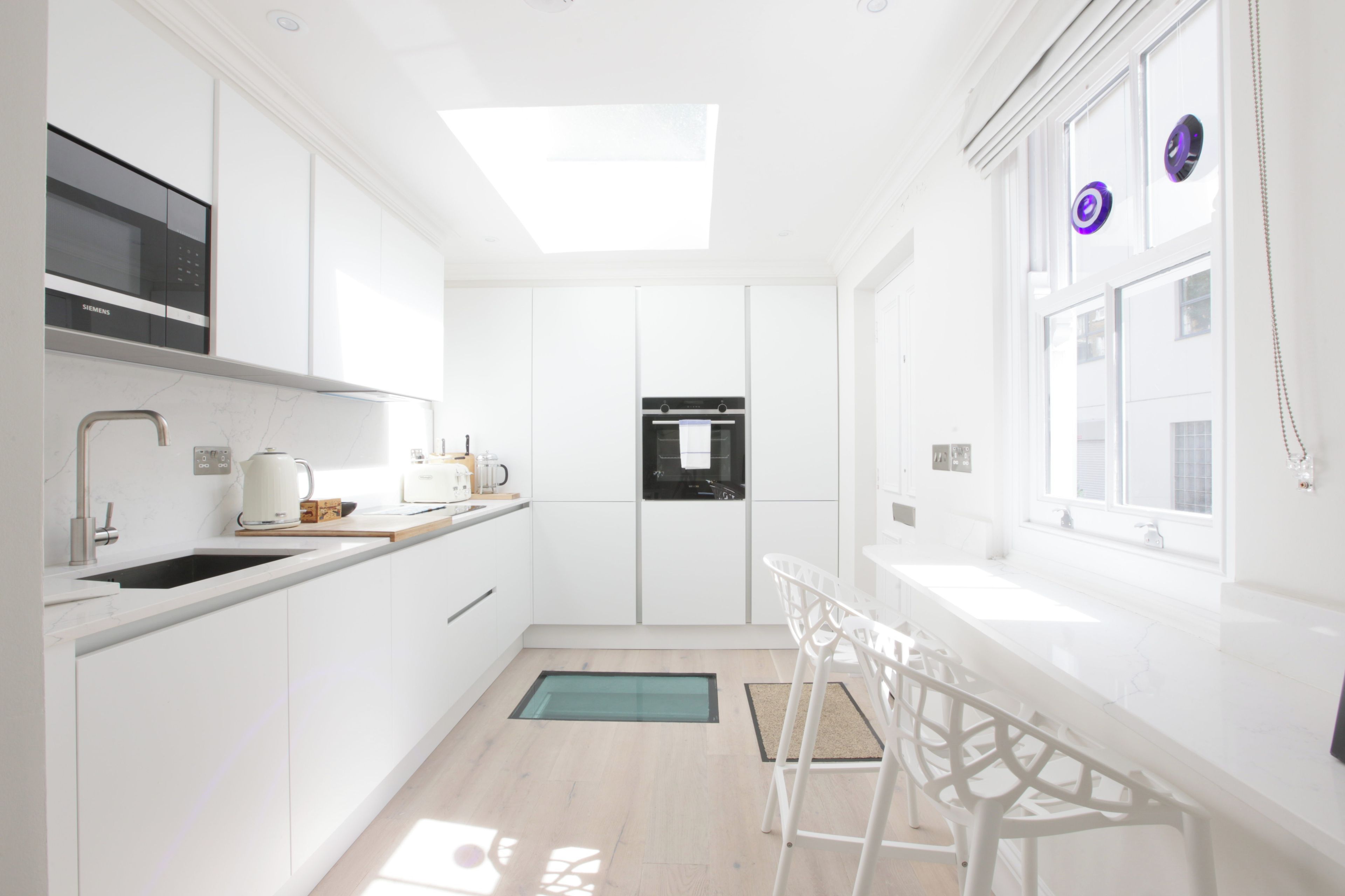 A modern kitchen with white cabinetry, a built-in oven, and a window with decorative elements.