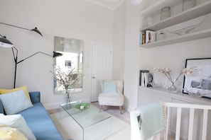Un salon moderne avec un canapé bleu, une table basse en verre, un fauteuil blanc et une bibliothèque agrémentée d’objets décoratifs.