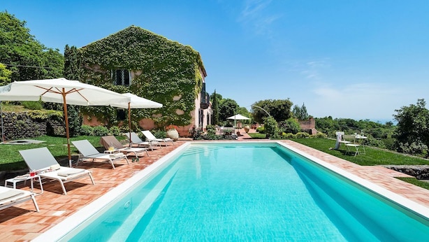 Une piscine rectangulaire à l’eau d’un bleu cristallin, entourée d’une terrasse en bois et de chaises longues blanches.