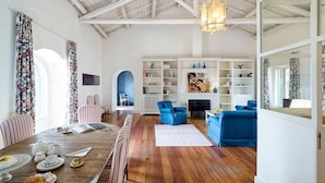 Un vaste salon doté d’un plancher en bois, d’une cheminée, d’une bibliothèque et d’un coin repas avec une table mise pour le repas.